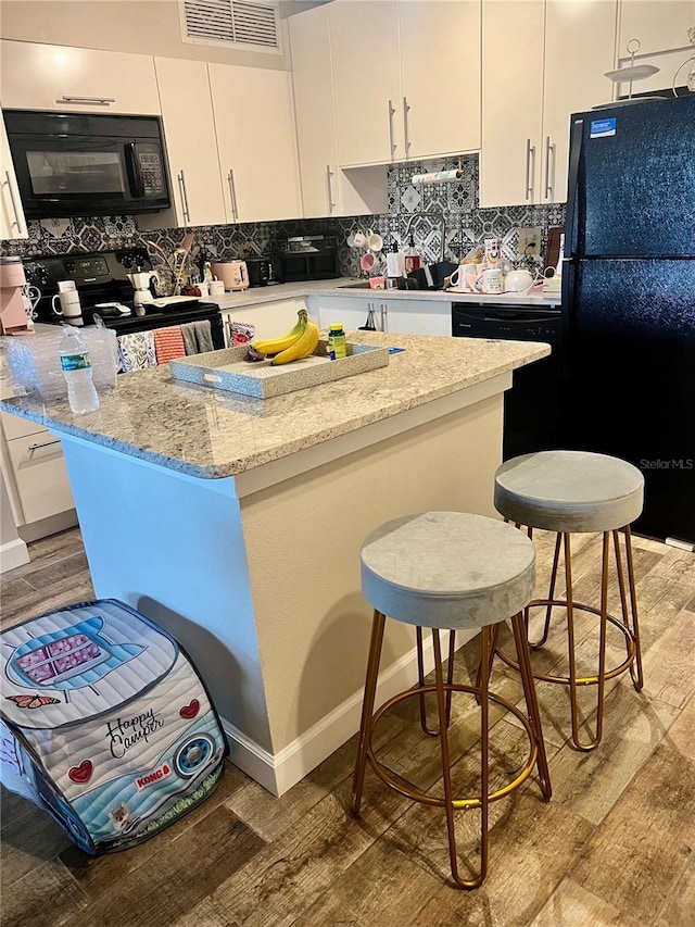 kitchen with black appliances, a kitchen breakfast bar, light wood-type flooring, and white cabinets