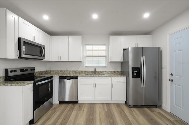 kitchen with appliances with stainless steel finishes, stone countertops, a sink, and white cabinetry