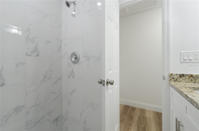 full bathroom with a tile shower, vanity, baseboards, and wood finished floors