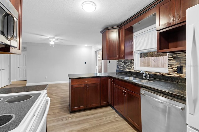 kitchen with kitchen peninsula, appliances with stainless steel finishes, light wood-type flooring, tasteful backsplash, and sink