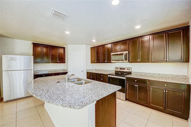 kitchen with stainless steel appliances, sink, a center island with sink, and light tile patterned floors