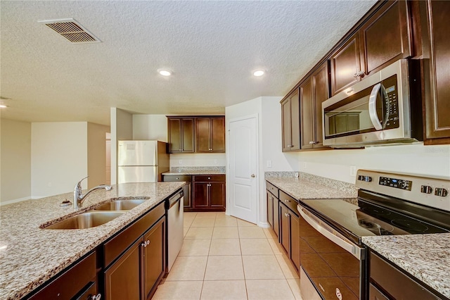 kitchen featuring light tile patterned flooring, sink, a textured ceiling, appliances with stainless steel finishes, and light stone countertops