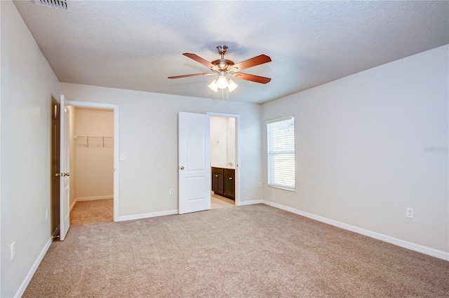 unfurnished bedroom with connected bathroom, a walk in closet, light carpet, a textured ceiling, and a closet