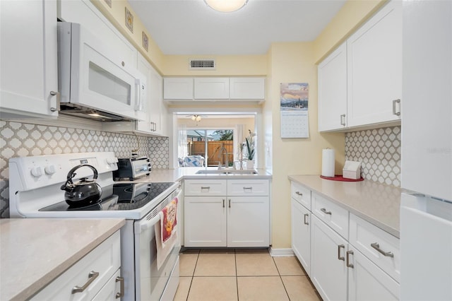 kitchen featuring white appliances, backsplash, sink, light tile patterned floors, and white cabinetry