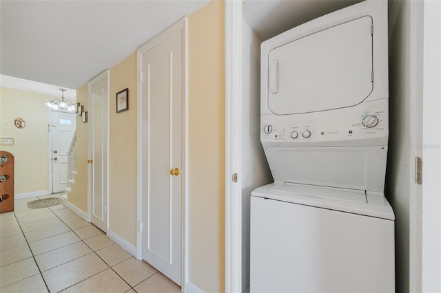 clothes washing area with light tile patterned floors, stacked washer and dryer, and an inviting chandelier