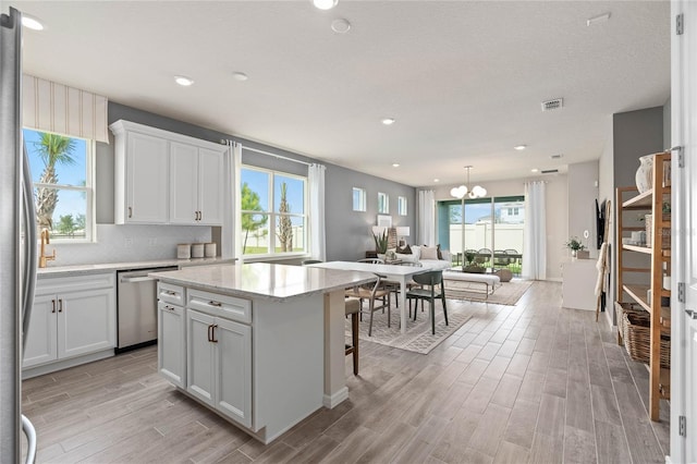 kitchen featuring pendant lighting, stainless steel dishwasher, light stone countertops, a kitchen island, and white cabinetry