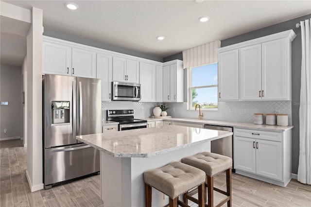 kitchen with a center island, a kitchen breakfast bar, light stone countertops, appliances with stainless steel finishes, and white cabinetry