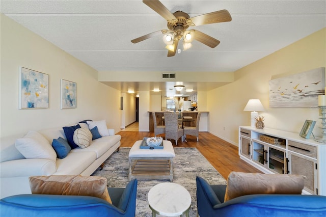 living room featuring ceiling fan, a textured ceiling, wood finished floors, visible vents, and baseboards