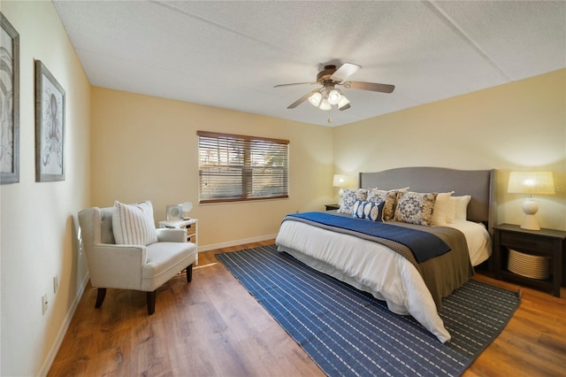 bedroom featuring ceiling fan, a textured ceiling, baseboards, and wood finished floors