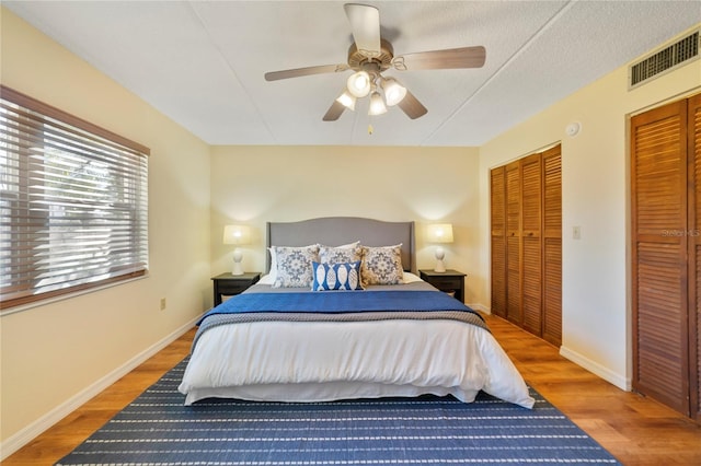 bedroom with multiple closets, baseboards, visible vents, and wood finished floors