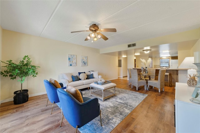 living area with visible vents, baseboards, light wood-style flooring, and a ceiling fan