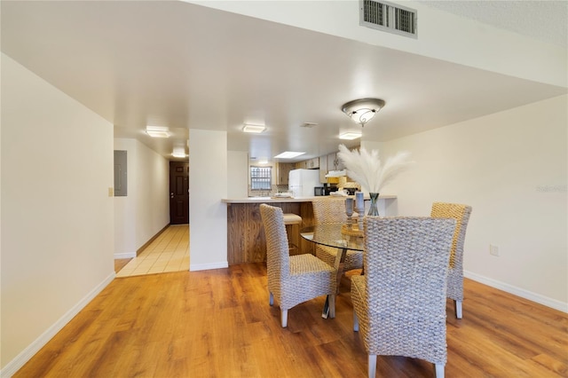 dining room with light wood-style floors, electric panel, visible vents, and baseboards