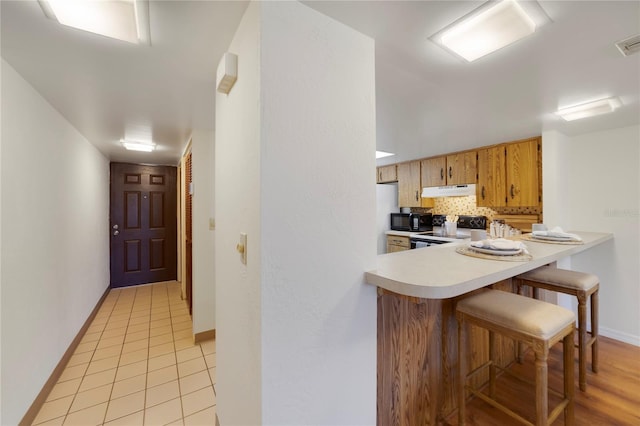 kitchen with white electric range oven, decorative backsplash, light countertops, under cabinet range hood, and black microwave