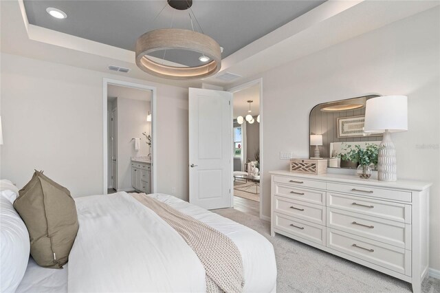 carpeted bedroom featuring a raised ceiling and ensuite bath