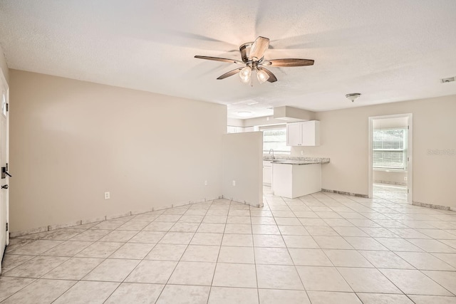 unfurnished living room with ceiling fan, light tile patterned floors, and a textured ceiling