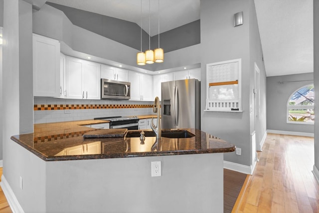 kitchen featuring white cabinetry, tasteful backsplash, dark stone countertops, appliances with stainless steel finishes, and kitchen peninsula