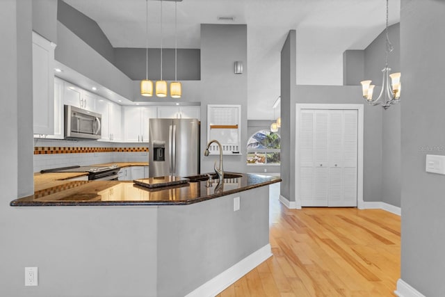 kitchen with stainless steel appliances, decorative light fixtures, kitchen peninsula, and dark stone counters