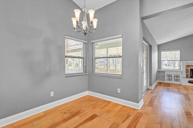 unfurnished dining area with wood-type flooring, a fireplace, a chandelier, and vaulted ceiling