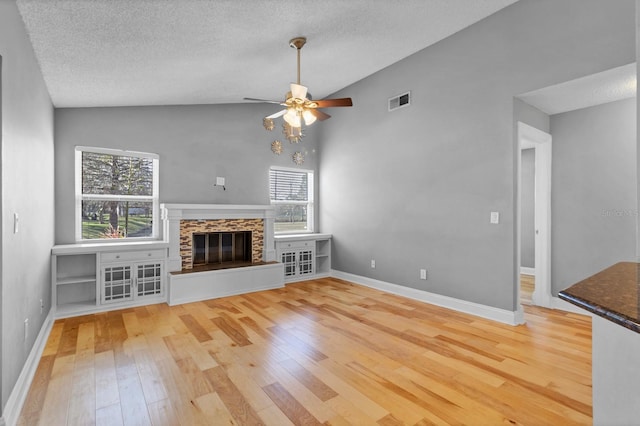 unfurnished living room with lofted ceiling, ceiling fan, a textured ceiling, a stone fireplace, and light wood-type flooring