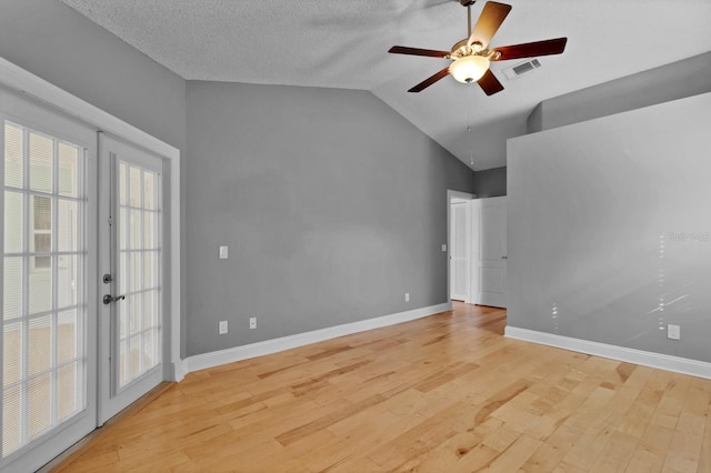 unfurnished room with vaulted ceiling, ceiling fan, a textured ceiling, light wood-type flooring, and french doors