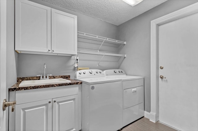 washroom with sink, cabinets, a textured ceiling, independent washer and dryer, and light hardwood / wood-style floors