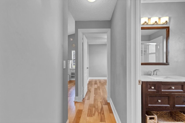 hallway with light hardwood / wood-style floors, sink, and a textured ceiling