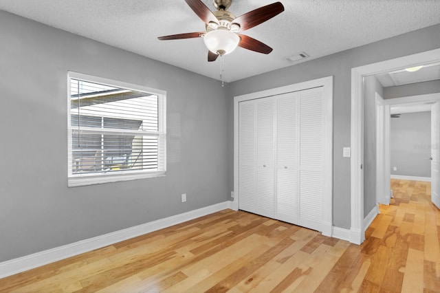 unfurnished bedroom with light wood-type flooring, a textured ceiling, ceiling fan, and a closet