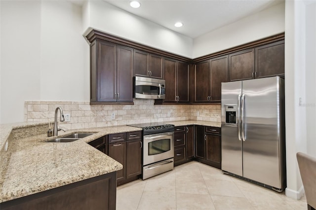 kitchen with sink, light tile patterned floors, light stone countertops, appliances with stainless steel finishes, and dark brown cabinetry