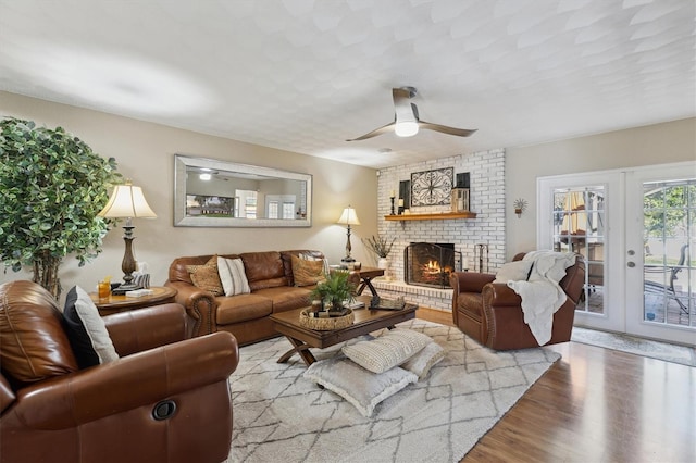 living room with a brick fireplace, ceiling fan, french doors, and light hardwood / wood-style flooring