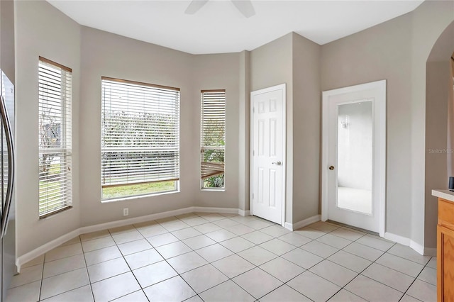 unfurnished bedroom with light tile patterned flooring, stainless steel fridge, ceiling fan, and a closet