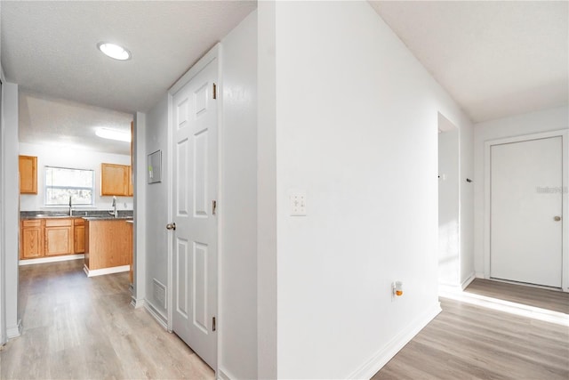 corridor with a textured ceiling, sink, and light hardwood / wood-style flooring