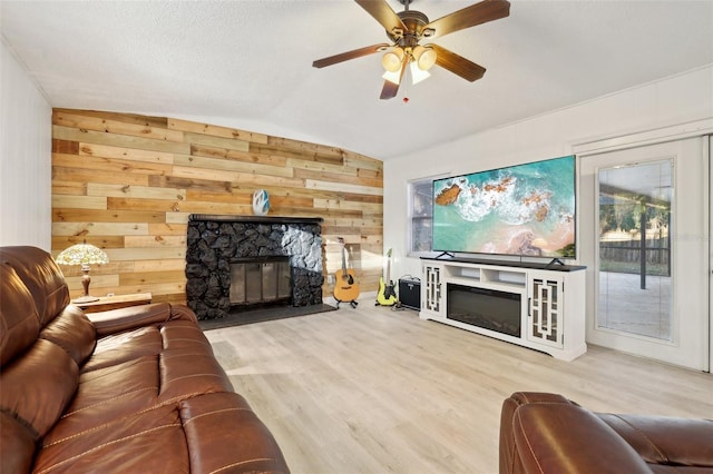 living room featuring wood walls, lofted ceiling, hardwood / wood-style flooring, ceiling fan, and a fireplace