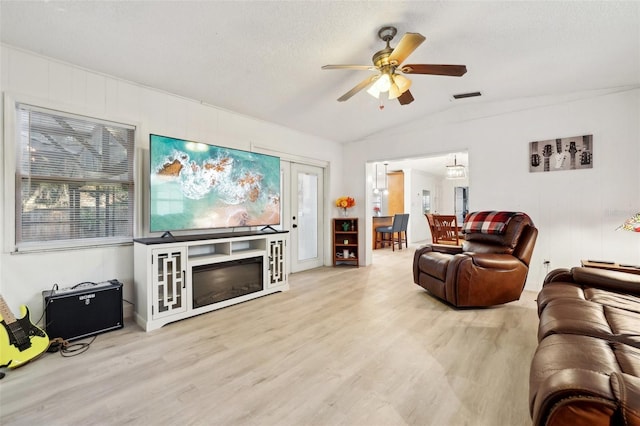 living room with ceiling fan, light wood-type flooring, a textured ceiling, and vaulted ceiling