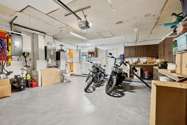 garage featuring electric panel, heating unit, a garage door opener, and washer / dryer