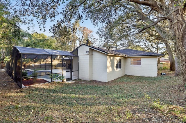 rear view of house featuring a lawn and glass enclosure