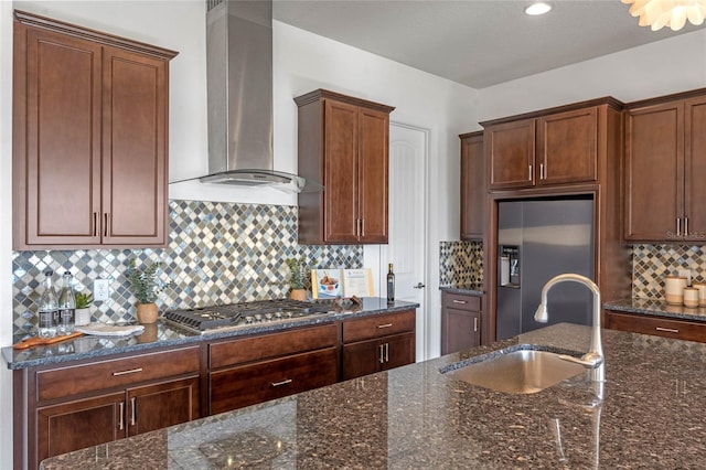 kitchen with wall chimney range hood, tasteful backsplash, dark stone counters, appliances with stainless steel finishes, and sink