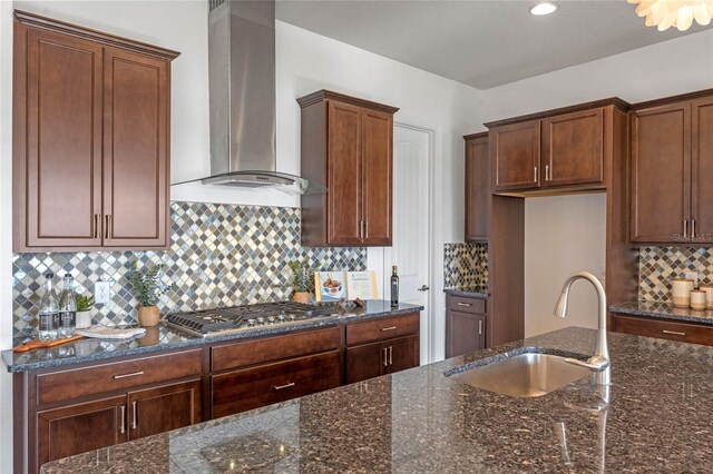 kitchen with sink, wall chimney range hood, stainless steel gas cooktop, and dark stone counters