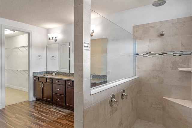 bathroom featuring hardwood / wood-style flooring, a textured ceiling, tiled shower, and vanity