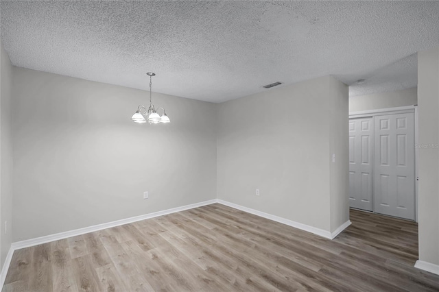 empty room with hardwood / wood-style floors, a textured ceiling, and a notable chandelier