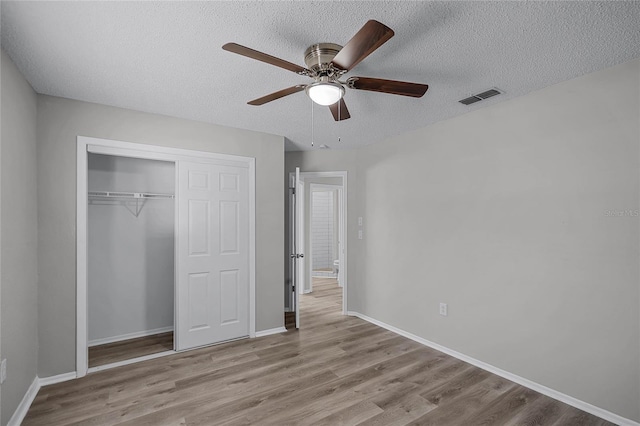 unfurnished bedroom with ceiling fan, light wood-type flooring, a textured ceiling, and a closet