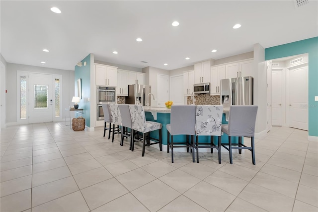 kitchen with a breakfast bar area, stainless steel appliances, decorative backsplash, a kitchen island with sink, and white cabinets