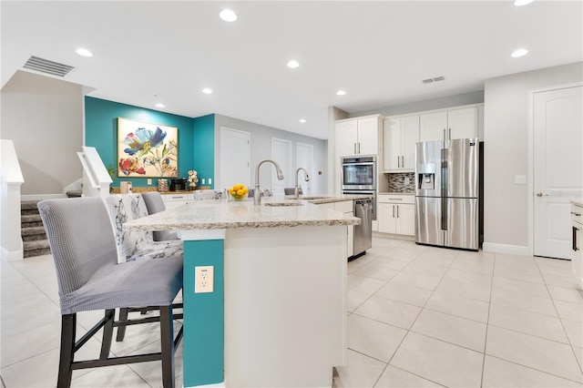 kitchen with light stone countertops, white cabinetry, stainless steel appliances, backsplash, and a kitchen island with sink