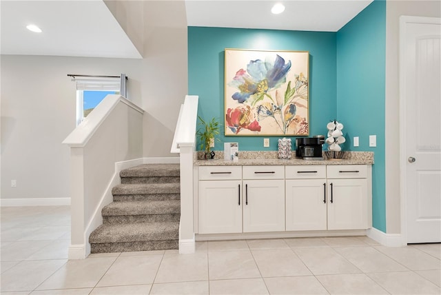 bar featuring light tile patterned flooring, white cabinetry, and light stone counters