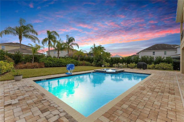 pool at dusk with a grill, a patio area, an in ground hot tub, and a lawn