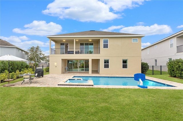 rear view of property with a lawn, a swimming pool with hot tub, a balcony, and a patio