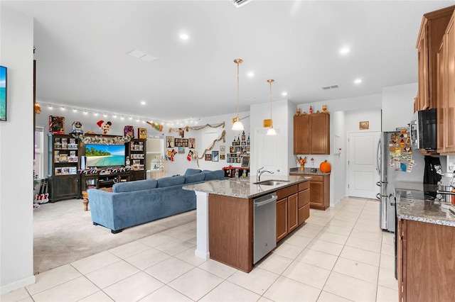 kitchen with hanging light fixtures, sink, an island with sink, appliances with stainless steel finishes, and light stone counters