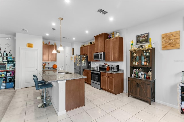 kitchen with light stone countertops, appliances with stainless steel finishes, a breakfast bar, a center island with sink, and light tile patterned flooring