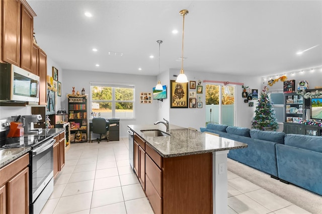 kitchen with stone counters, sink, stainless steel appliances, pendant lighting, and a kitchen island with sink