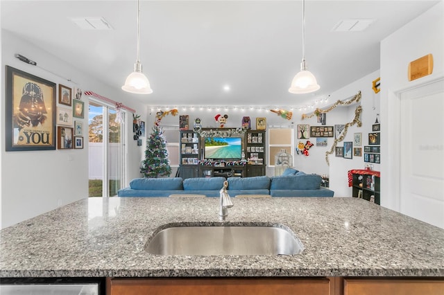 kitchen featuring light stone countertops, sink, hanging light fixtures, and a center island with sink