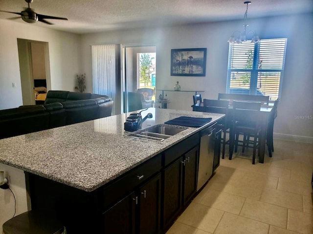 kitchen with pendant lighting, dishwasher, a kitchen island with sink, ceiling fan with notable chandelier, and sink